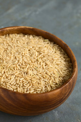 Raw brown or wholegrain rice kernels in wooden bowl, photographed on slate with natural light (Selective Focus, Focus one third into the rice)
