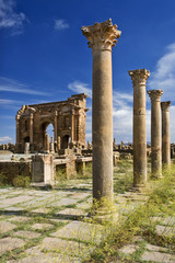 Fototapeta premium Algeria. Timgad (ancient Thamugadi or Thamugas). View on Trajan's Arch via the Sertius market with stone stalls surrounded by Corinthian columns