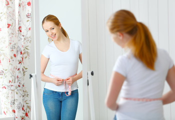 woman measuring waist  in front of mirror