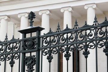 Naklejka premium Metal decorative fence. / Decorative metal fence on the background of the colonnade of the facade of the building.
