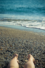 Female legs on the pebble coast of sea. Selective focus. Toned