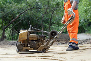 Worker in orange overalls with a plate compactor