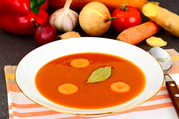 Carrot Tomato Soup in Plate. Behind lie on the soup ingredients,