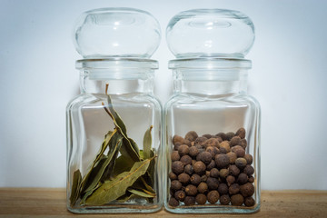 Bay leaves and allspice in a glass jar on the wooden shelf