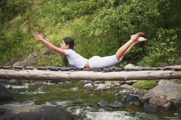 Beautiful young woman meditating in yoga pose at a mountain stream. Selective focus on woman.