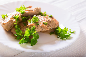 Fried meat with parsley greens on a white plate. There is on white boards, a close up, a horizontal shot