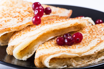 Fresh pancakes on a black plate with red berries
