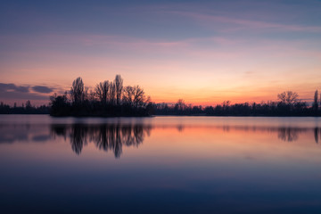 Obraz premium Farbiger Sonnenuntergang mit Wasserspiegelungen am See