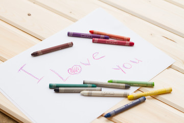 Разноцветные пастельные мелки (карандаши) и надпись на белом листе бумаги на английском "I love you"  