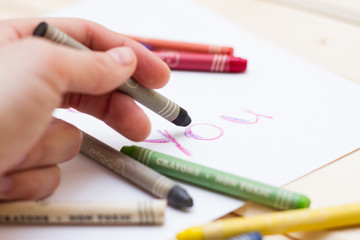 Разноцветные пастельные мелки (карандаши), надпись на белом листе бумаги на английском "you"  и рука с карандашом