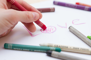 Разноцветные пастельные мелки (карандаши), надпись на белом листе бумаги на английском "love"  и рука с карандашом