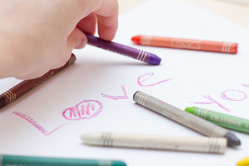 Разноцветные пастельные мелки (карандаши), надпись на белом листе бумаги на английском "love you"  и рука с карандашом