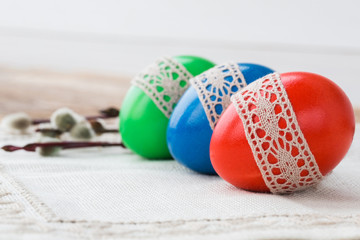 Three colorful Easter eggs on white tablecloth. Copy space, selective focus