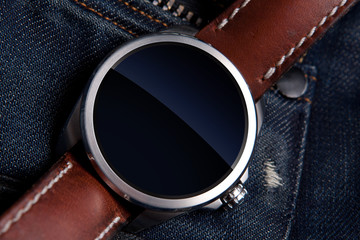 Smart watch concept on matte and polished metal case with brown leather strap on blue jeans...