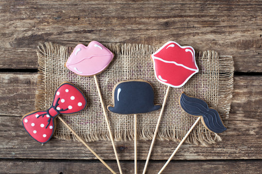 Homemade gingerbreads in the form of photobooth props (mustache, lips, the bow tie and cylinder) on the wooden table. Space for text and selective focus. - Powered by Adobe
