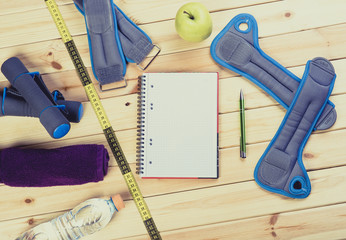 Sport Equipment. Dumbbells,  Ankle Weights, Wrist Weights, Towel, Tape Measure, Bottle Of Water, Notebook To Workout Plan On Wooden Table. Sport Fitness Background