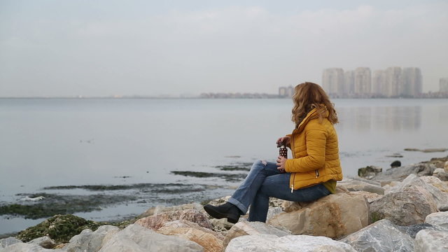 Woman sitting alone in rocks on the seaside bank and be lonely, rainly day