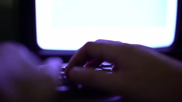 Hacker like scene where person is typing quickly on keyboard, strange lighting to set the mood of hacking.