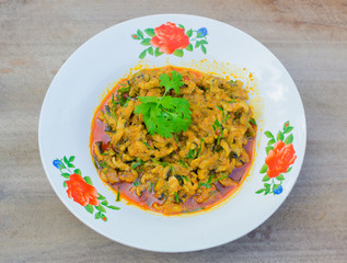Spicy curry fresh fish with herb topping in white dish on wood background.