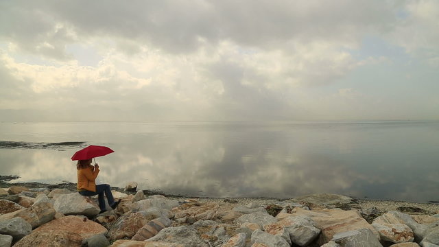 Lonely woman with umbrella,  sitting on the rock at the seashore