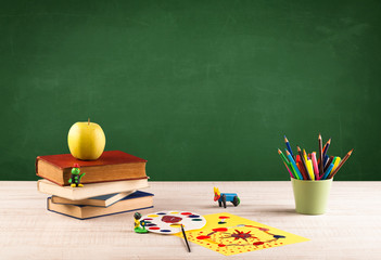 School items on desk with empty chalkboard