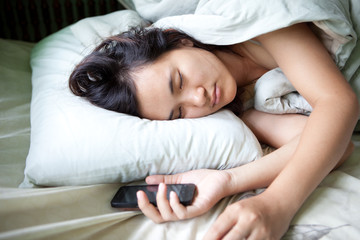 Obraz na płótnie Canvas Sleeping Young woman holding a smart phone like smartphone addiction