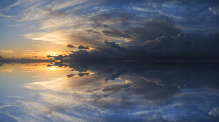 Large vibrant panorama image of stormy sunset sky with reflectio