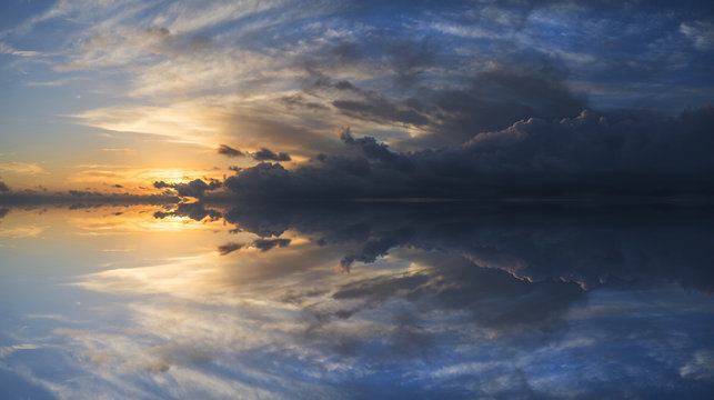 Large vibrant panorama image of stormy sunset sky with reflectio