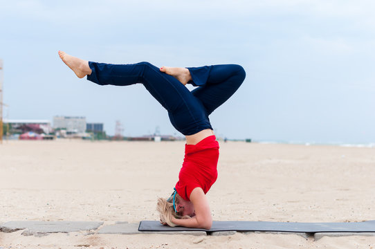 Beautiful young fit woman doing sport exercises, variation of supported headstand posture, salamba sirsasana, side view, coast on gray background