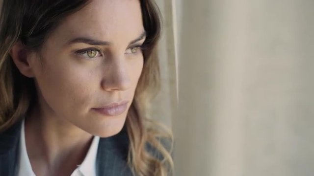 Portrait of young business woman in a hotel room by the window looking far away with a worried look. Extreme close up.