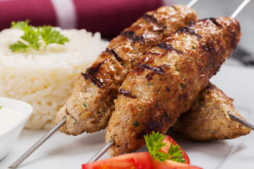 Barbecued kofta - kebeb with rice and vegetables on a plate.