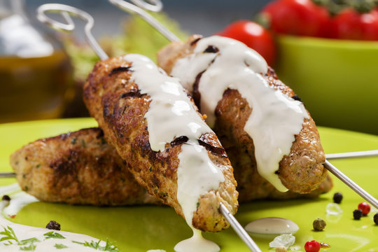 Barbecued kofta - kebeb topped with sauce with vegetables on a p