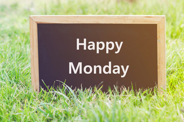 Happy Monday note on blackboard on green grass.