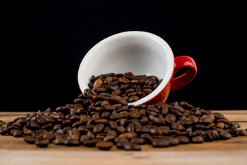 Coffee beans in red cup on wooden table with black background.