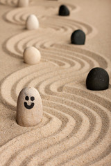 Stone smiley sticking out of the sand, between white and black stones