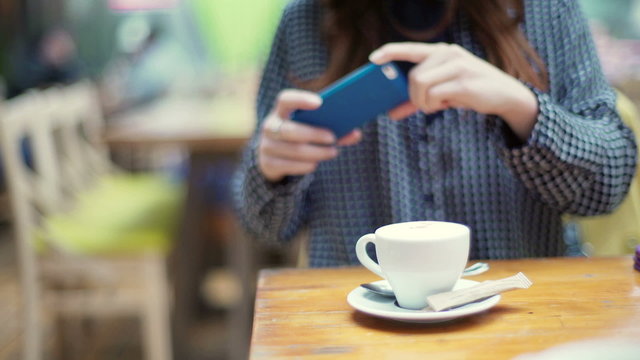 Girl sitting in the cafe and doing photo of cup on smartphone
