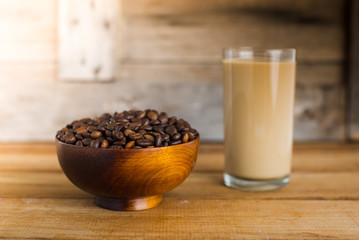 Coffee beans in bowl and a glass of coffee milk on wooden table.