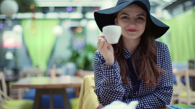 Glamorous woman drinking beverage and smiling to the camera in the cafe
