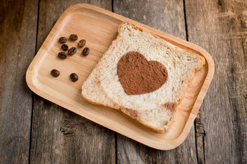 Cocoa powder forming a heart on a bread on wooden background.