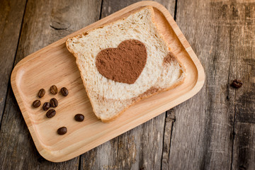 Cocoa powder forming a heart on a bread on wooden background.