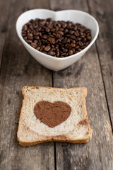 Bread slice with heart shape and coffee beans in white bowl on w