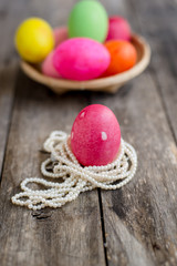 Pink easter egg on pearl necklace and wooden background.