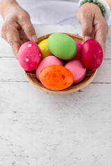 Hands holding easter eggs basket on wooden table with copyspace.