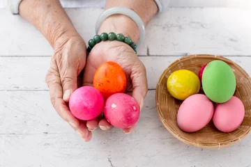 Fensteraufkleber Hands holding easter eggs basket on wooden table. © nuiiko
