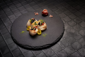 Haute cuisine scallops served on black plate. 