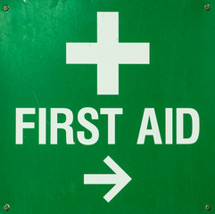 Green metal First aid Sign screwed to a wall and pointing towards the first aid room