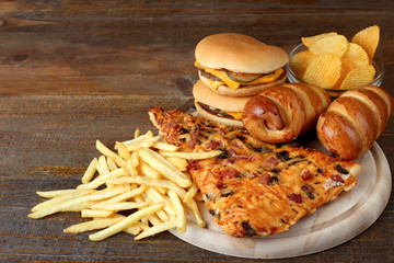 a large piece of delicious pizza and a hamburger with fries on a wooden chopping Board on brown...