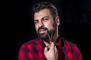 Man with red plaid shirt trimming his beard with scissors