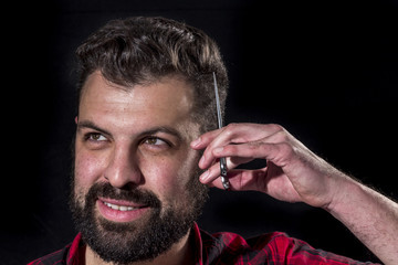 Crazy bearded young scratching his head with scissors