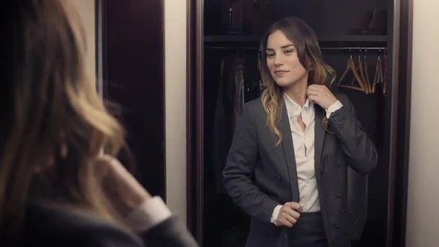 Confident business woman gets ready in front of a mirror, looking at herself happy. She smiles and leaves.